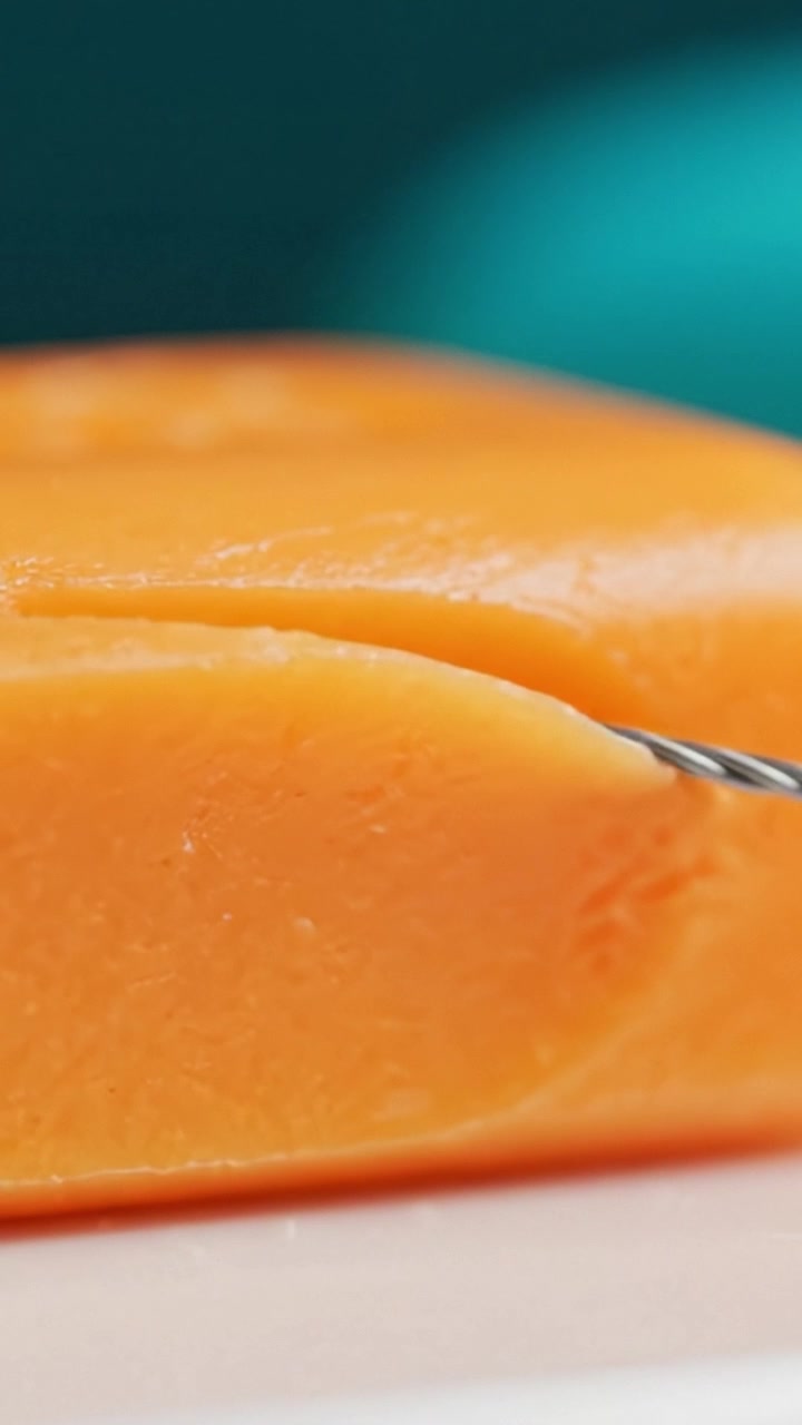Una Vista Ravvicinata di Delizioso Formaggio Arancione Affettato con un Tagliaformaggio a Filo, Evidenziandone la Consistenza e la Freschezza in un Contesto Culinario
