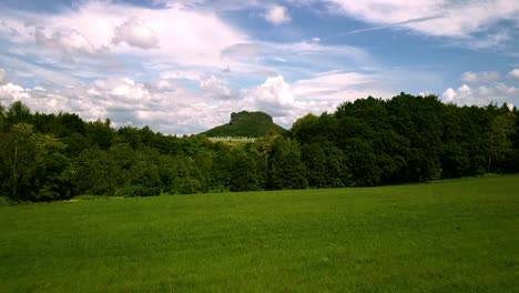 Drone-flight-starting-low-and-climbing-higher-over-green-fields-towards-an-iconic-mountain-rock-formation-in-saxony-Europe-on-a-bright-sunny-day