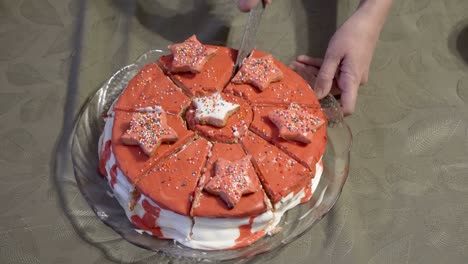 a close-up of a beautiful cake that a woman cuts into equal pieces with a knife. the cake is decorated with red icing and cookies in the form of stars. the concept of a home holiday. top view. 4k.