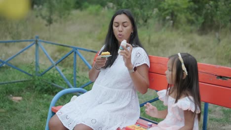 una madre embarazada y su hija joven disfrutan de un tiempo de juego juntos en un patio de recreo en el parque, rodeados de árboles y vegetación
