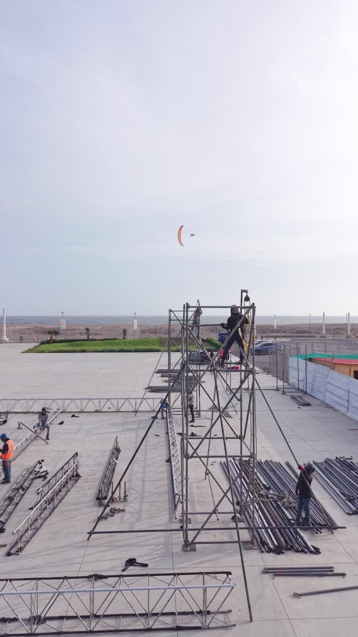 Construction Workers Assembling Metal Scaffolding Near the Ocean with Paraglider Flying