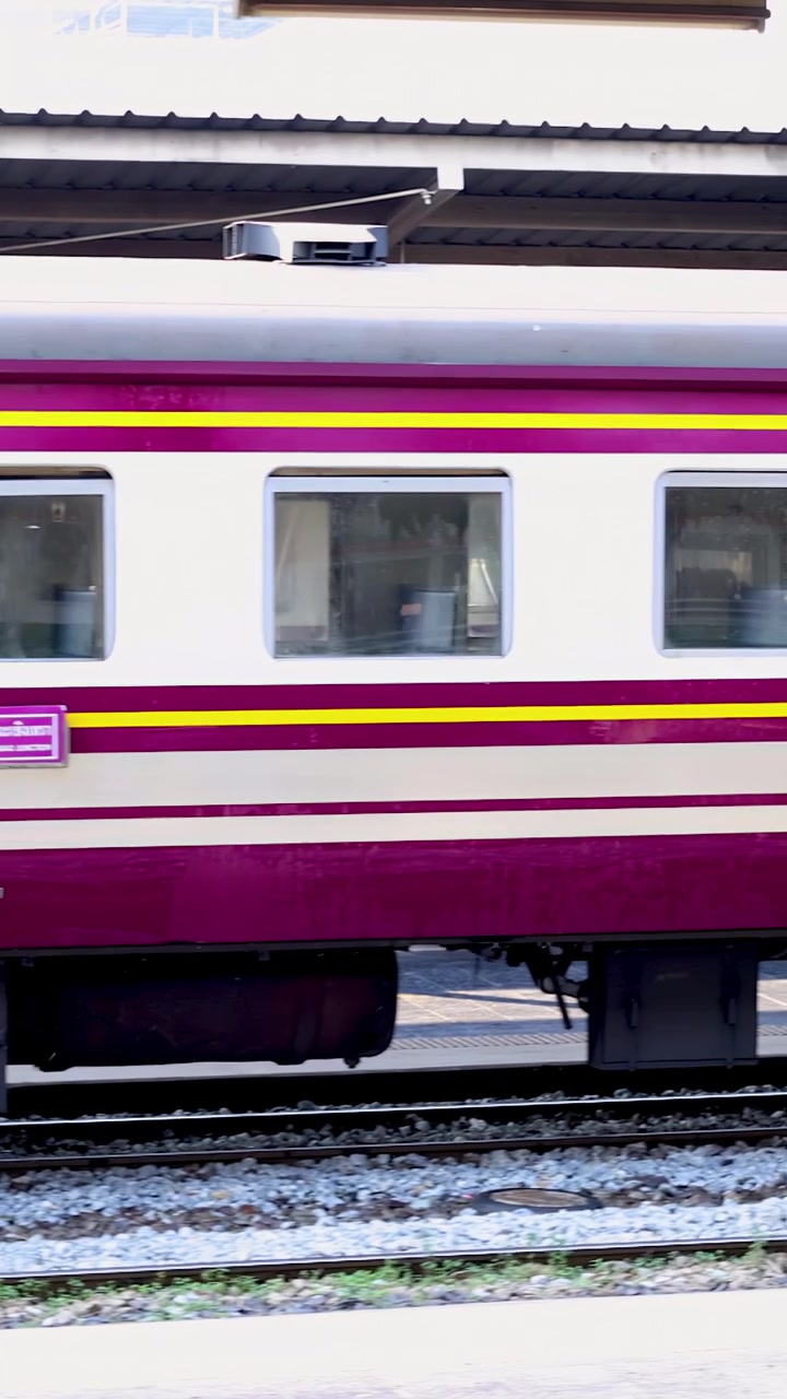 Petugas perawatan menyemprotkan air di sepanjang kereta penumpang merah marun di peron stasiun kereta api Bangkok yang terang.