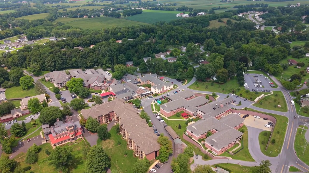 Ripresa aerea con drone dall'alto che mostra una zona residenziale di una piccola città con case, prati e la chioma degli alberi.