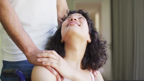 Happy-biracial-woman-in-wheelchair-and-smiling-to-male-partner-in-sunny-living-room