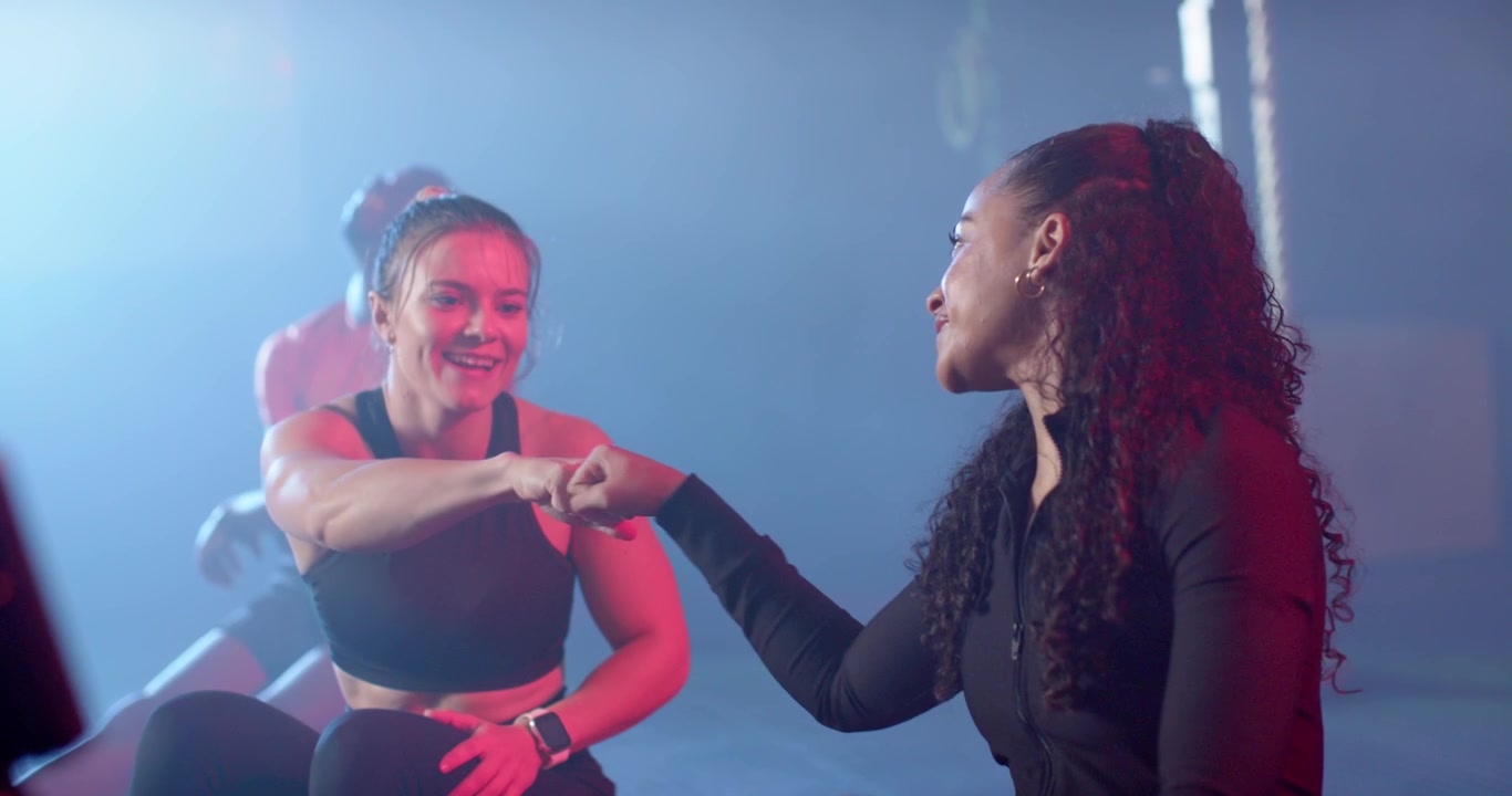 African American woman finishing set in gym, celebrating fist bump handshake with friend with watch