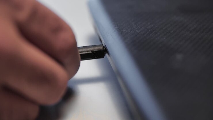 Hand connecting an audio cable to a laptop's audio jack