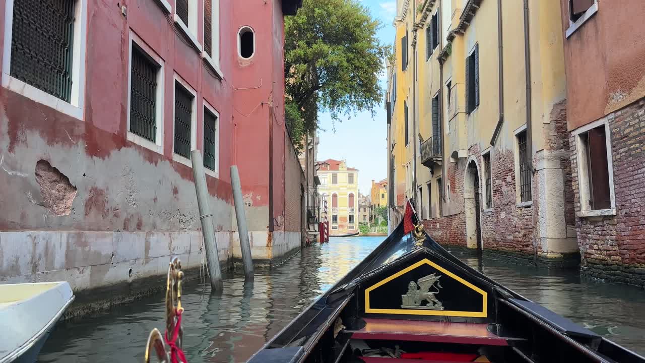 Una gondola scivola attraverso gli stretti canali di Venezia con edifici colorati in una giornata di sole