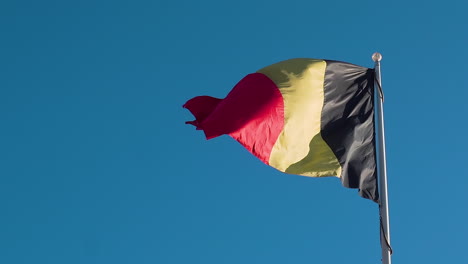 the national flag of belgium on a flag pole waving against the blue sky