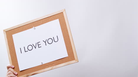 Woman's-hand-shows-the-paper-on-board-with-the-word-I-LOVE-YOU-in-white-studio-background-with-copy-space