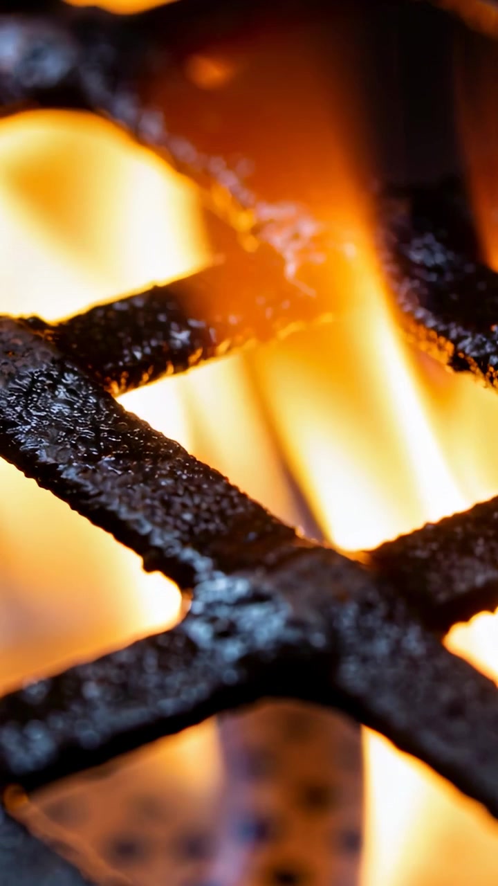 Video verticale: Fiamme alimentate dal gas che tremolano attraverso una griglia del bruciatore carbonizzata sul piano cottura della cucina, fuliggine.