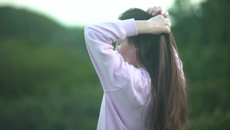 자연 속에서 그녀의 부드럽고 매끄러운 머리를 가지고 노는 여자의 중간 샷