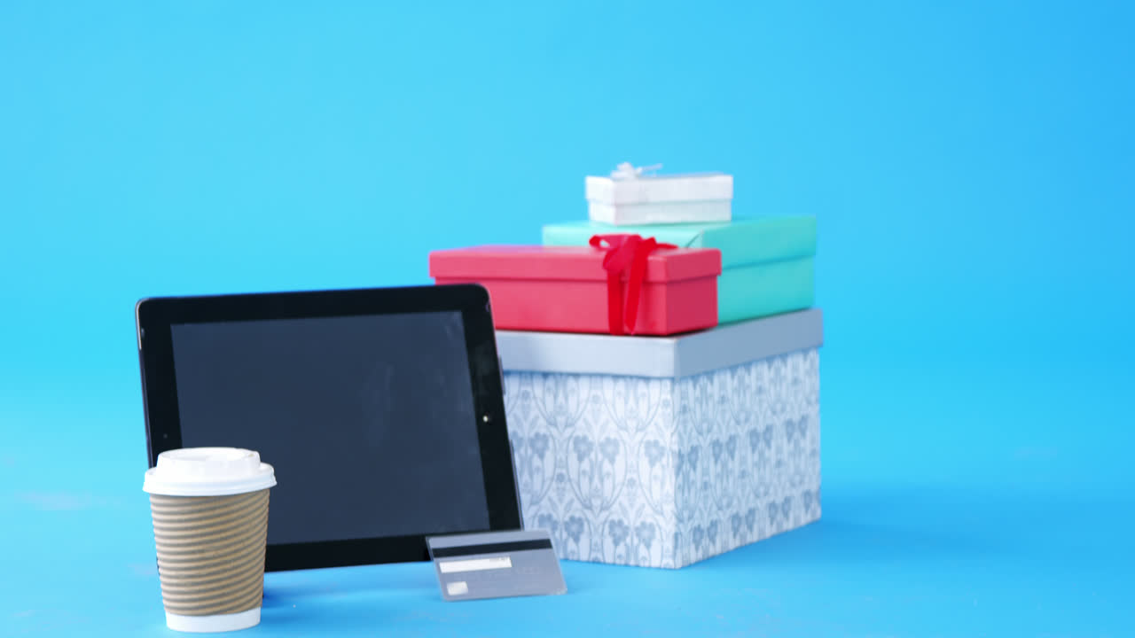 tarjeta de crédito, caja de regalos, taza de café desechable y tableta digital sobre fondo azul