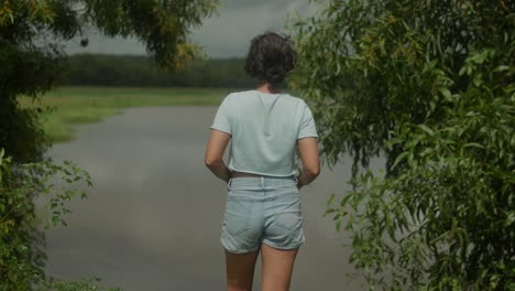 slow-motion shot of an attractive young girl stands by the edge of a serene lake in a natural park