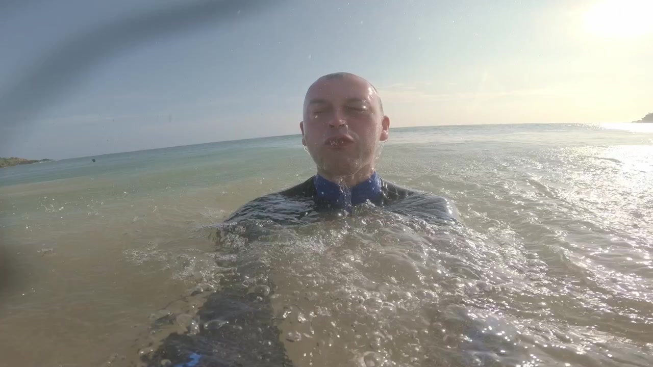 Filmato ravvicinato a livello dell'acqua mostra un uomo adulto mentre un'onda tropicale crescente sommerge la action camera, riempiendo l'obiettivo di bolle prima che riappaia tra le onde illuminate dal sole vicino a Mirissa, Sri Lanka