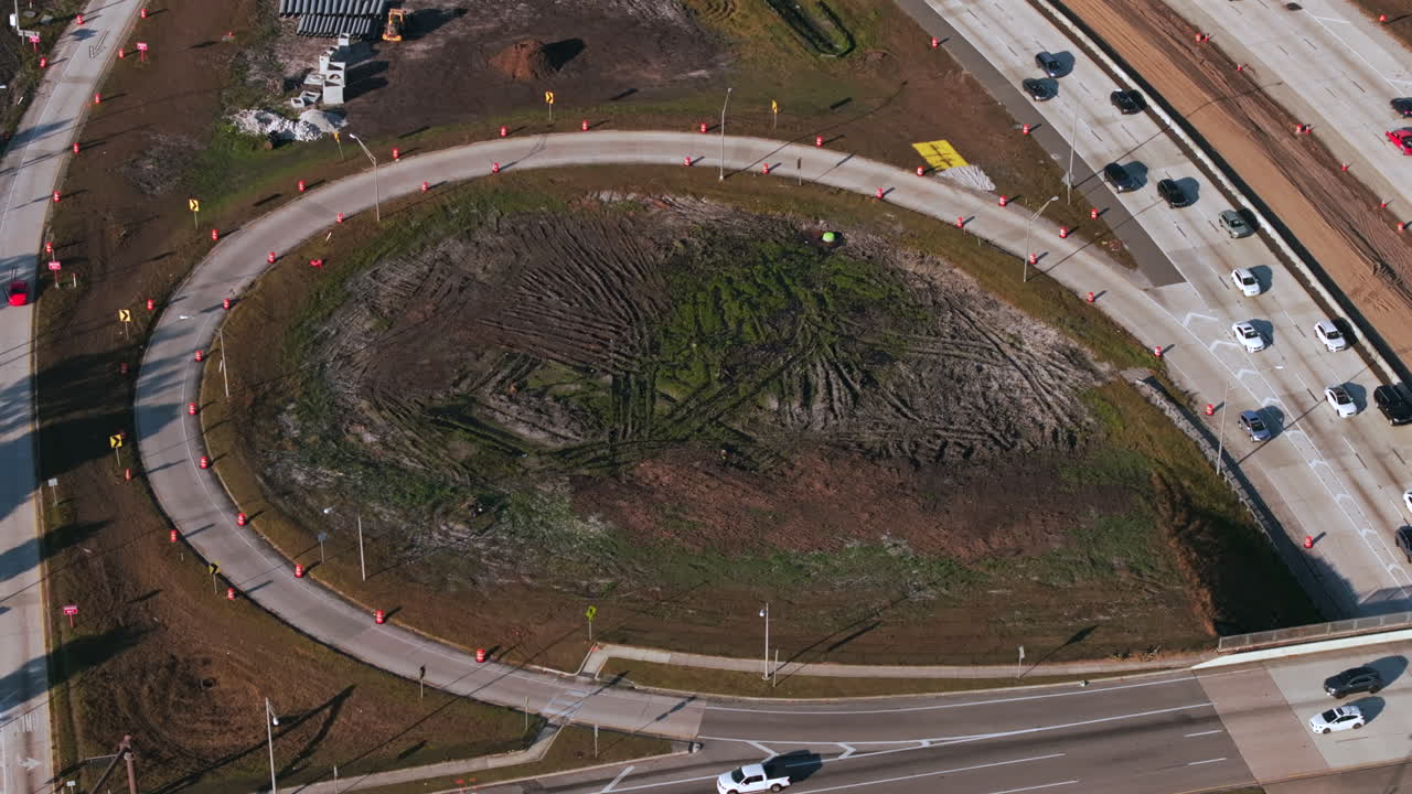 Zdjęcie z lotu ptaka pod dużym kątem przedstawia pętlę autostrady w budowie, ukazując złożony proces rozbudowy nowoczesnej infrastruktury transportowej