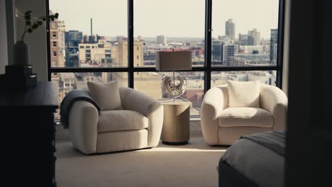 push in shot of a sitting area in the primary bedroom of a home with comfy white chairs and large windows behind