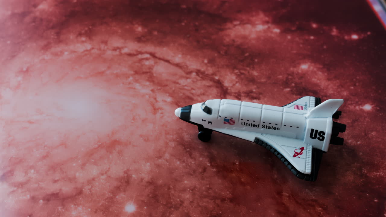 Close up of a miniature toy space shuttle placed on a reddish galaxy background