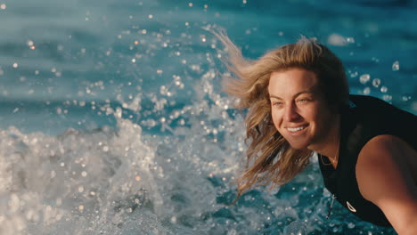 Blonde-female-wake-surfer-smiling-as-she-rides-perfect-wave-on-blue-lake-water-at-golden-hour-in-slow-motion