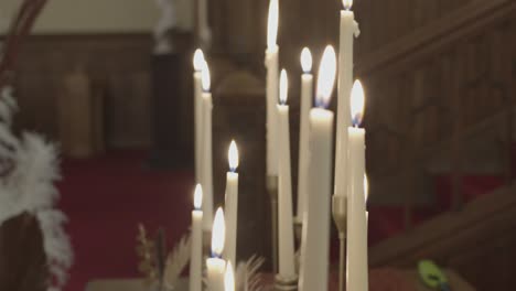 panning close-up of a bunch of white candle sticks burning brightly with a blurred event space in the background