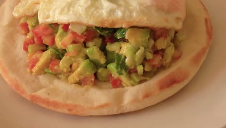 Close-up-pedestal-shot-of-a-pita-bread-topped-with-avocado-salad-and-one-fried-egg-for-a-healthy-vegetarian-keto-breakfast