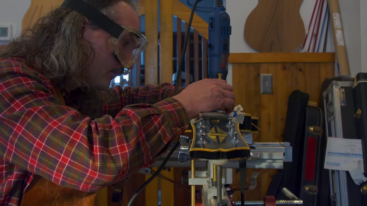 Tilt up to guitar technician refretting electric guitar on jig in shop