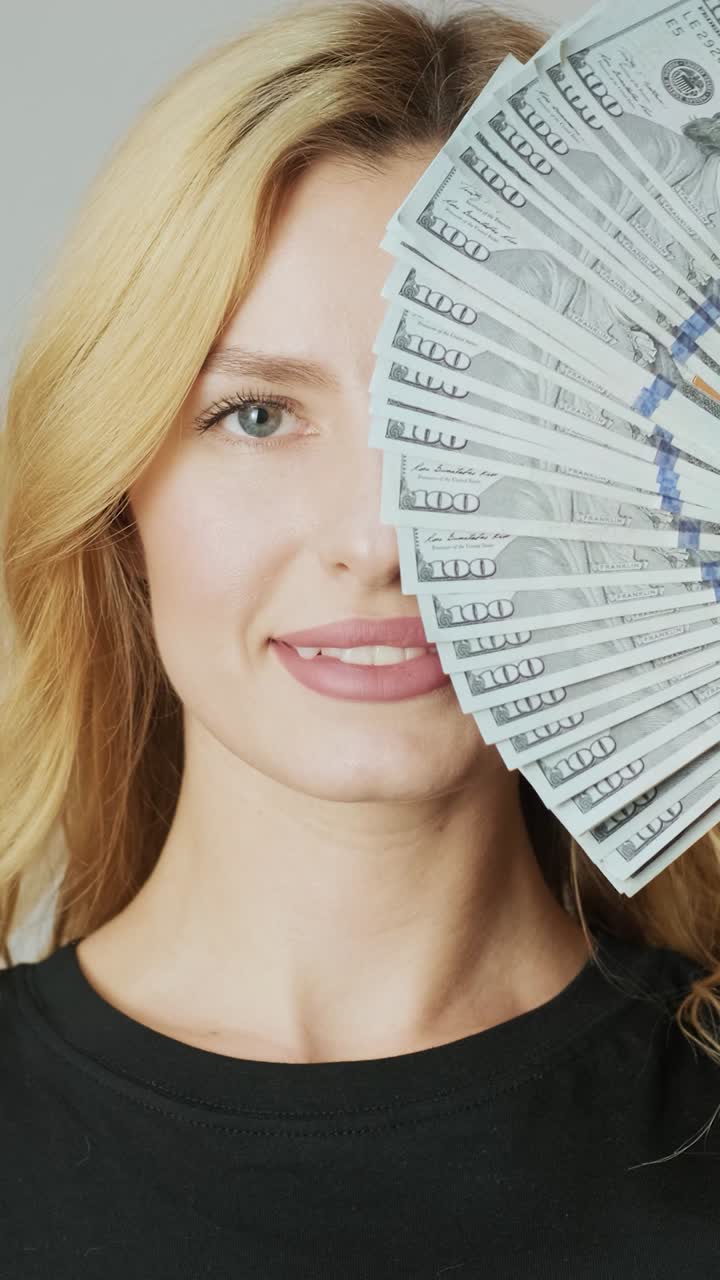Giovane donna che tiene un ventaglio di banconote da cento dollari davanti al suo volto.