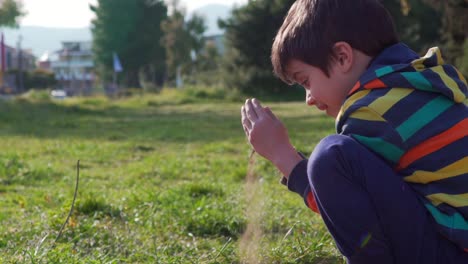 Niño-Caucásico-Jugando-En-El-Campo,-Agachándose-Y-Soltando-Tierra-De-Sus-Manos,-Cámara-Lenta-De-120-Fps