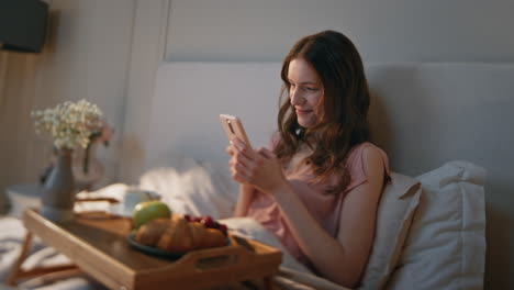 home girl using smartphone in cozy bedroom closeup. relaxed smiling woman look