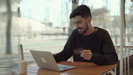 Un-Joven-Feliz-Sosteniendo-Una-Tarjeta-De-Crédito-Y-Usando-Una-Computadora-Portátil