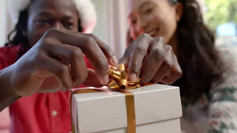 happy diverse couple sticking bow on christmas gift at home, slow motion