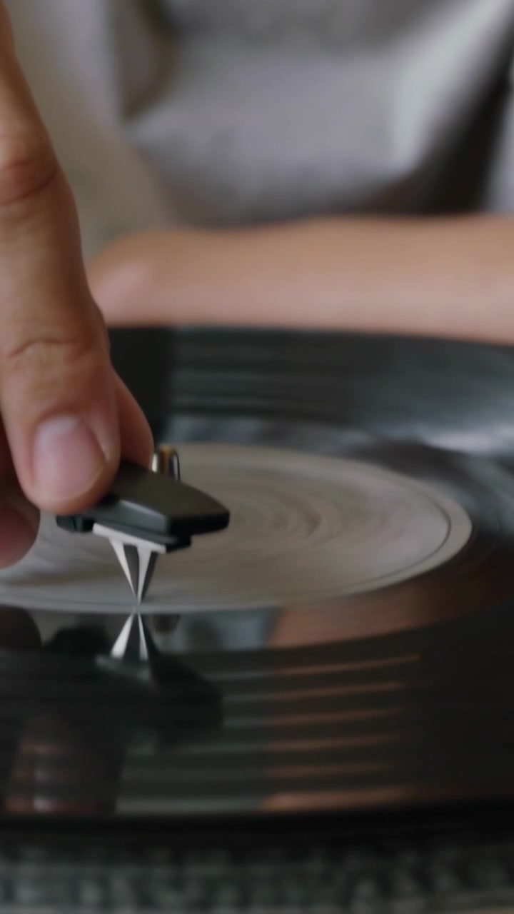 Video verticale: Adolescente in felpa girocollo grigia in primo piano che abbassa lo stilo sul vinile sul giradischi a casa per riprodurre
