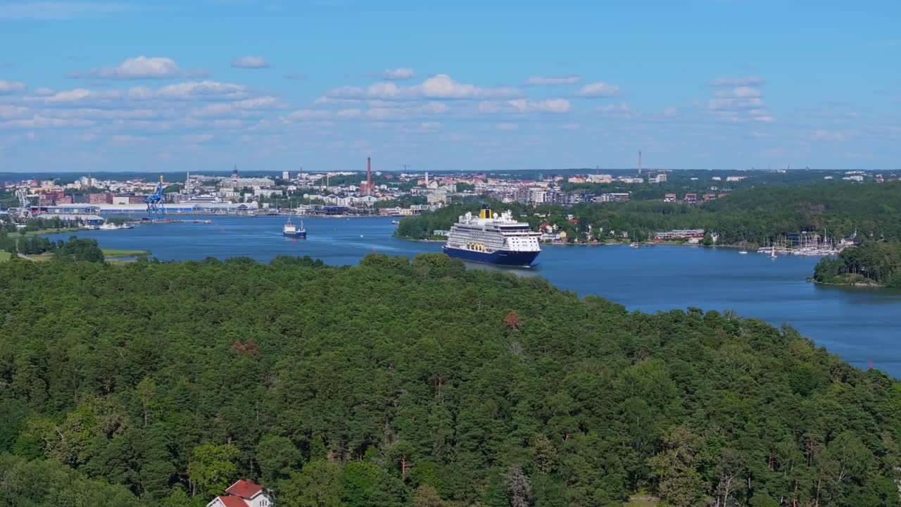 SAGA Cruise ship SPIRIT OF ADVENTURE navigating narrow archipelago fairway in Finland on departure. City in background. Distant aerial front view.