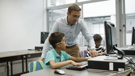 boy in eyeglasses asking teacher about computer assignment and then typing on keyboard