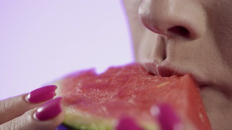 mujer comiendo sandía en primer plano, esmalte de uñas femenino y labios de lápiz labial rojo en fondo rosa