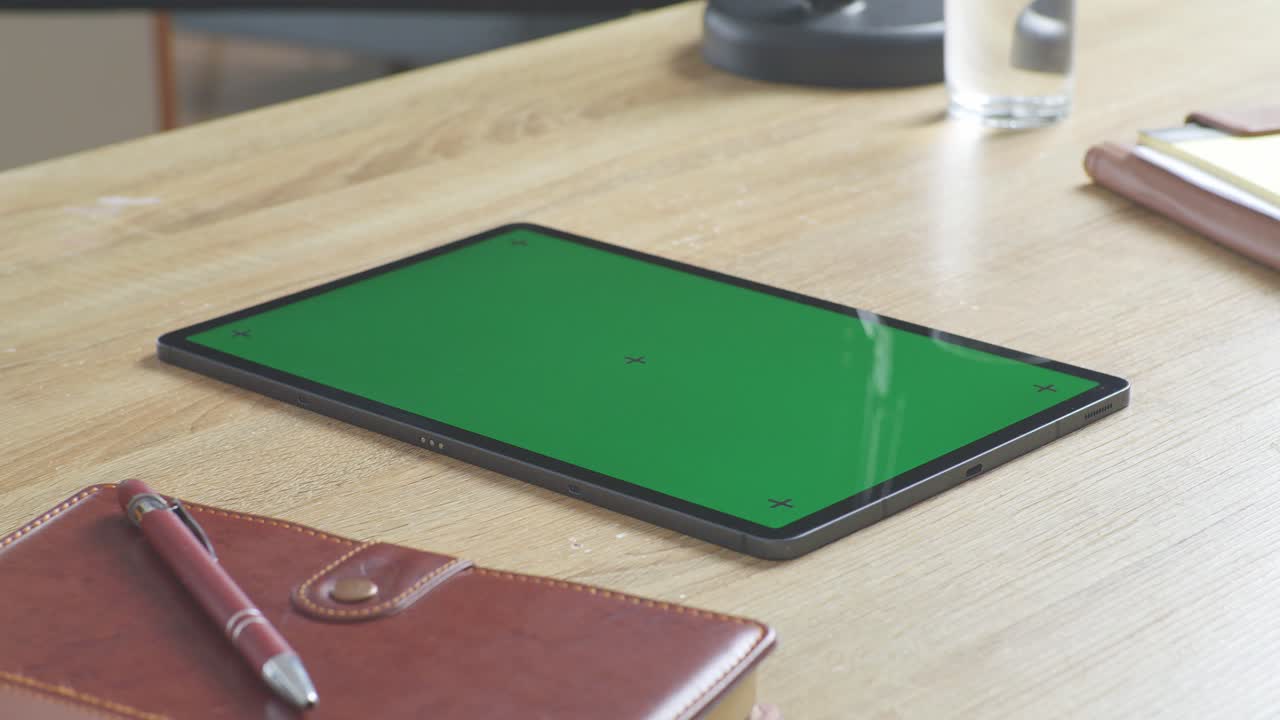 vista de arriba hacia abajo de una computadora portátil con pantalla verde simulada pantalla chromakey en un escritorio de oficina de madera al lado de la libreta con bolígrafos, gafas y un vaso de agua.