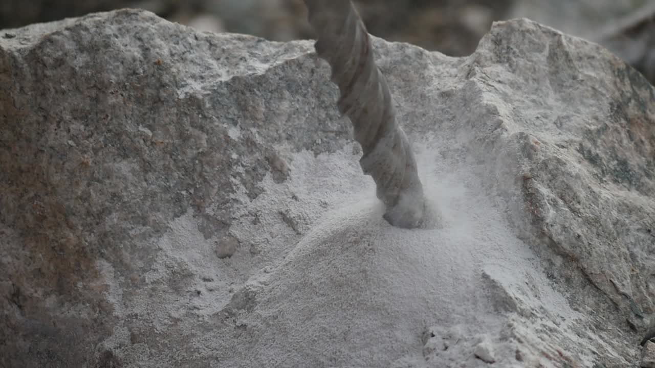 Close up of a driller digging a hole into a rock producing smoke and sand in slow motion