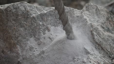 close up of a driller digging a hole into a rock producing smoke and sand in slow motion