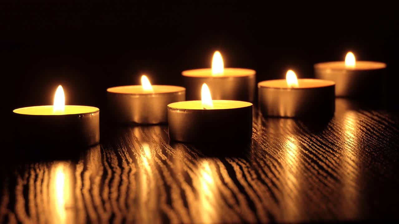 La candela tremola nel buio. Una candela bianca e rotonda brucia su uno sfondo scuro. Candele rotonde bruciano e si spengono. Dolore. Romanticismo. Gioia. Video 4K.