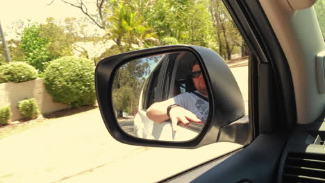 man looks out of window seen in rear view mirror left side of vehicle