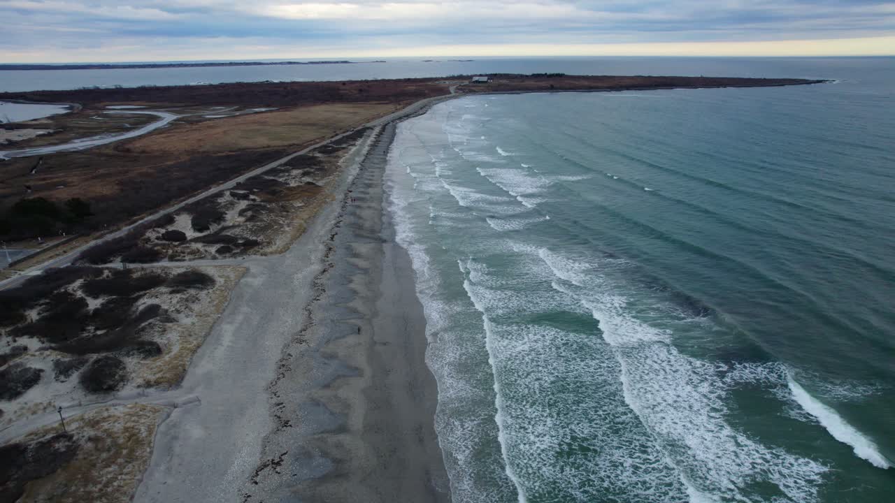 Luftfoto av havbølger som sakte slår inn på en strand en skyet dag