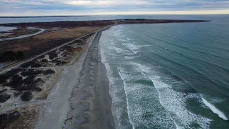 aerial of ocean waves slowly crashing on a beach on a cloudy day