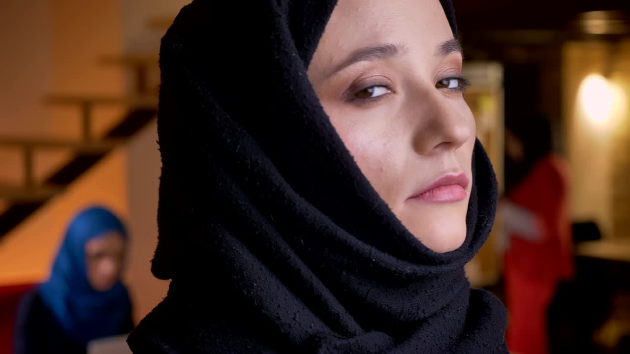 retrato de una joven mujer musulmana hermosa que trabaja en una oficina con hijab negro mirando hacia el lado y dirigiéndose a la cámara