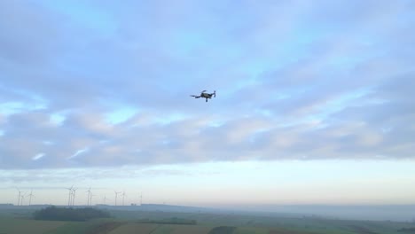 Drone-Filmando-Un-Drone-Volando-Contra-El-Cielo-Con-Nubes-Sobre-El-Paisaje-Rural-Al-Atardecer
