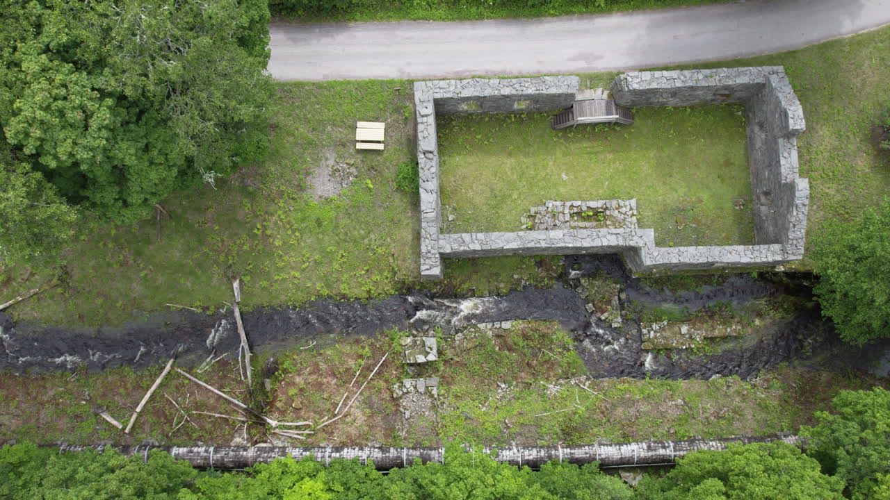Top-down aerial view of stone ruins and a flowing stream surrounded by greenery at Bäckefors Bruk, Sweden