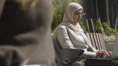 mujer de negocios musulmana sentada al aire libre en los jardines de la ciudad trabajando en una computadora portátil 1