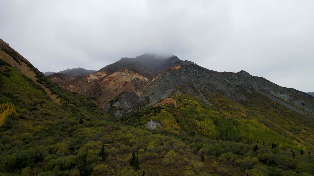 montaña colorida con una capa de nubes rodeada de pinos y arbustos verdes en alaska