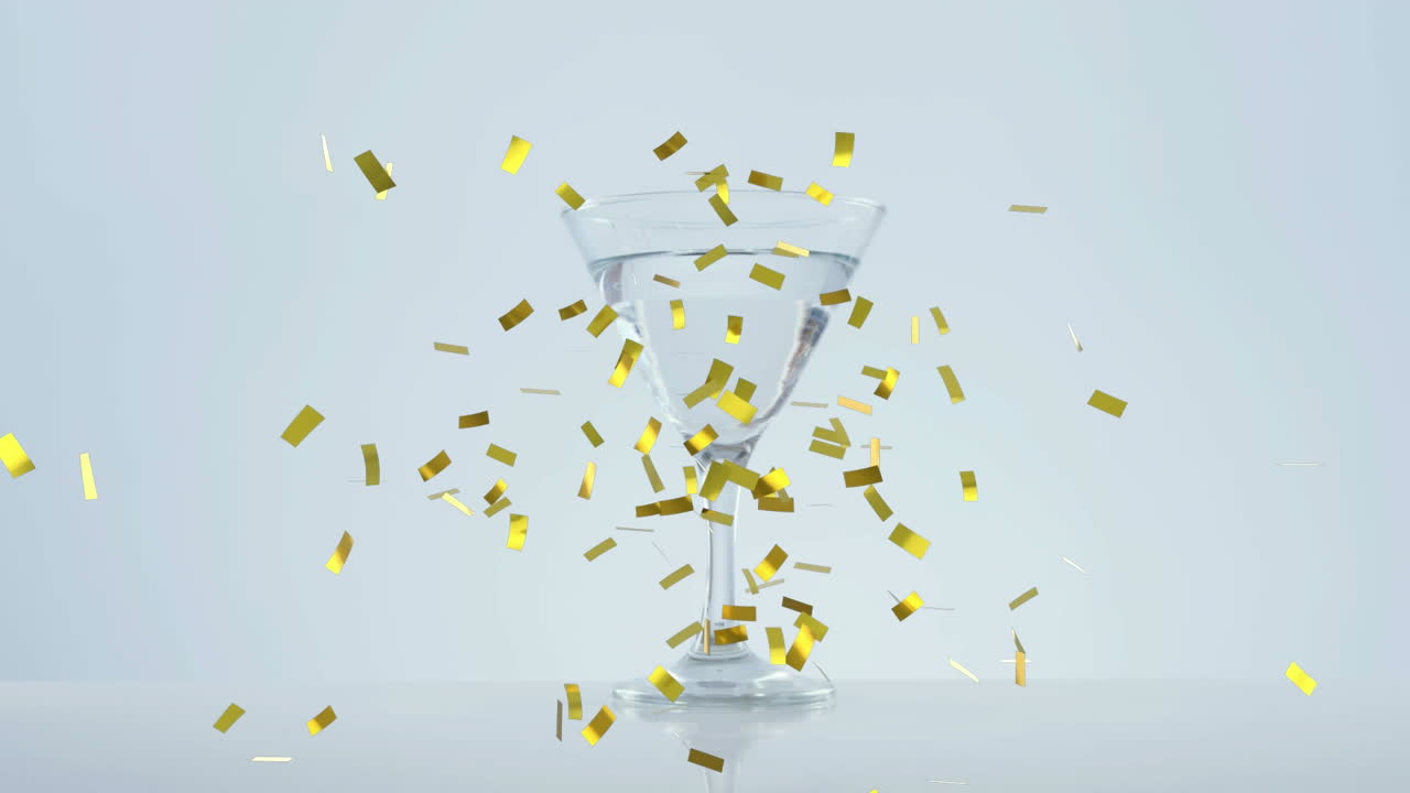 Golden confetti falling over olives falling into cocktail glass against grey background