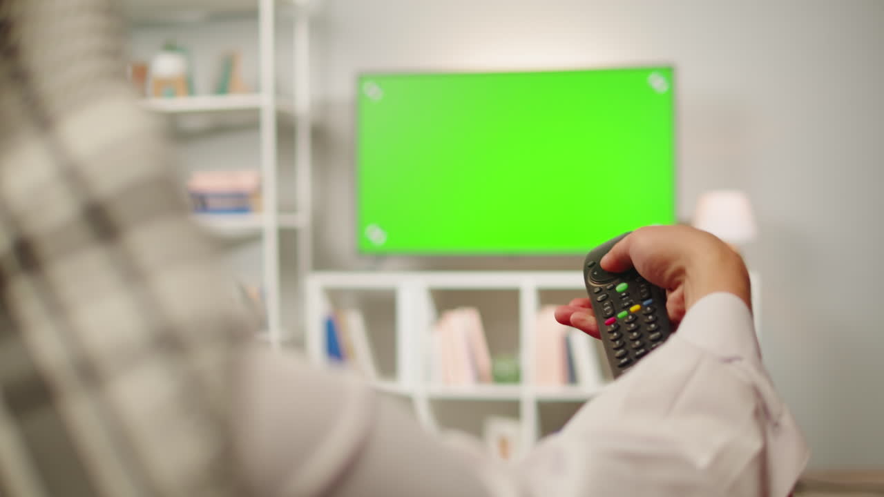 Middle eastern man watching tv with chroma key close-up. Person watches television with green screen in living room. Wearing traditional Islamic clothes
