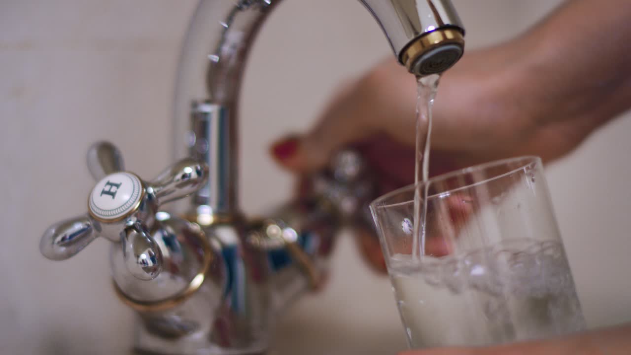 mujer con la mano vertiendo agua en el vaso del grifo de agua en la cocina