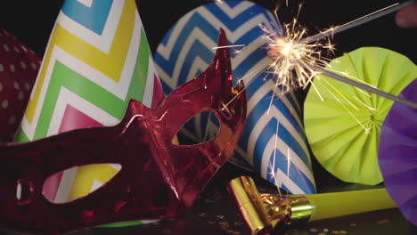 party hats, carnival mask, sparkler and colorful decorations on black background